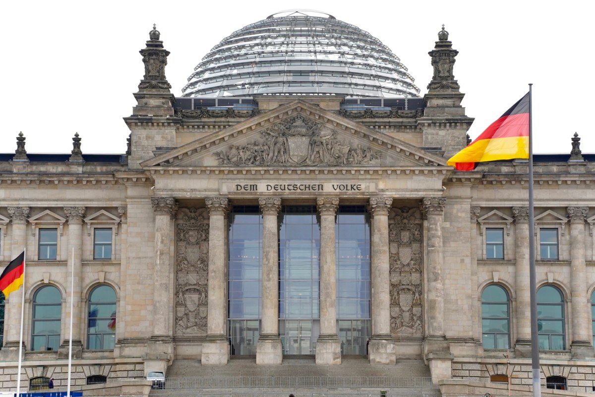 Flagi Polski i Niemiec powiewające przed budynkiem Bundestagu w Berlinie, symbolizujące debatę o relacjach między oboma krajami.