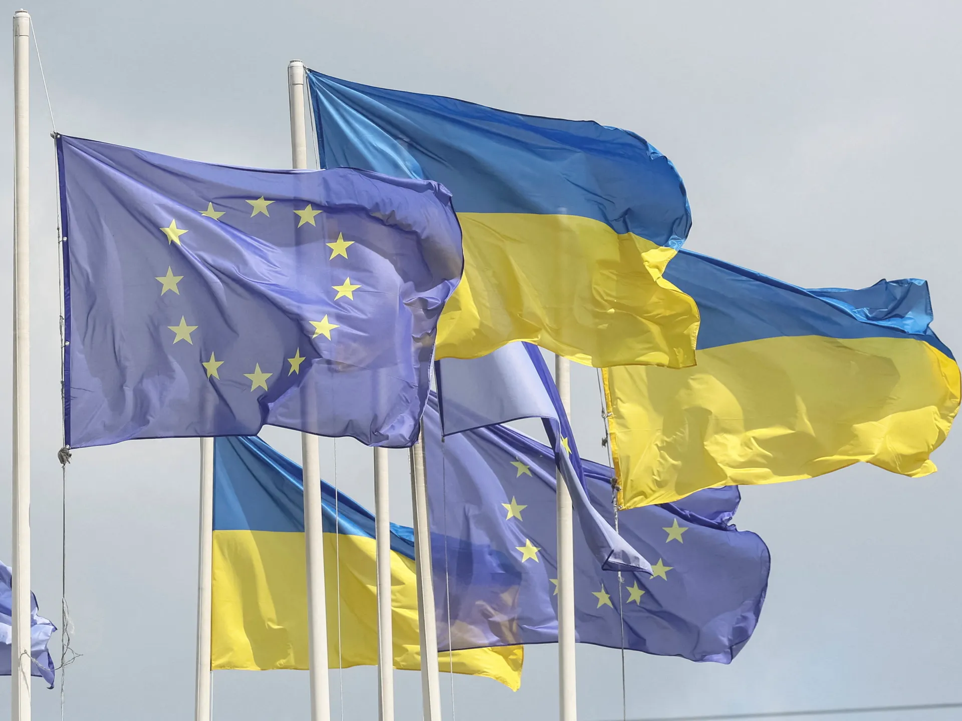 Flagi Unii Europejskiej, Ukrainy i Mołdawii powiewające razem przed gmachem instytucji europejskiej.