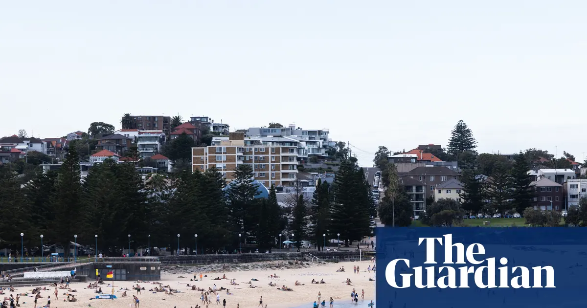 Widok na spokojną plażę Coogee w Sydney w słoneczny dzień, z oddali widać ocean i ludzi spacerujących brzegiem.