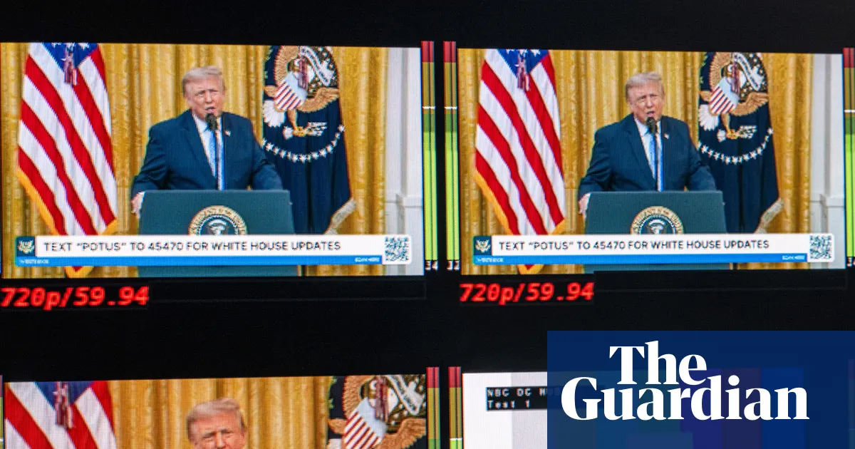 Donald Trump przemawia za mównicą, w tle ekrany telewizyjne przedstawiające podział relacji medialnych.