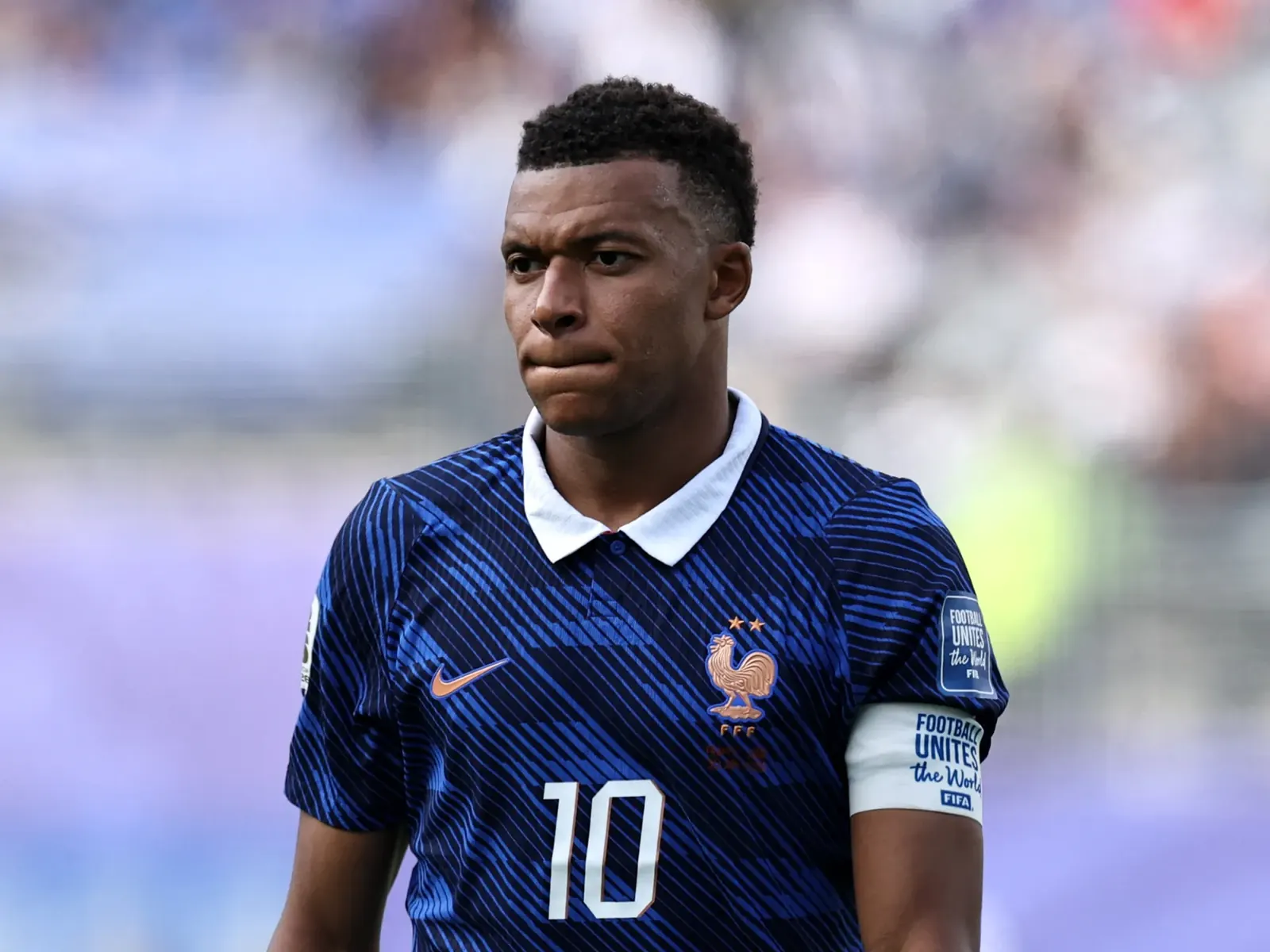 Kylian Mbappé na boisku piłkarskim, obok portret senator Celeste Amarilli