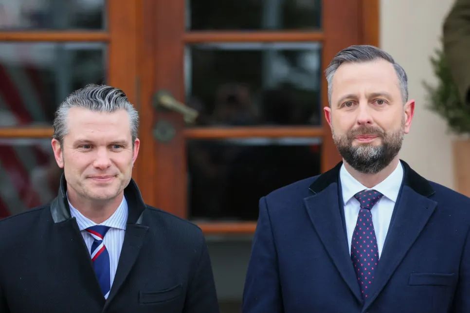 Władysław Kosiniak-Kamysz rozmawiający z Pete'em Hegsethem na tle flag NATO i USA.