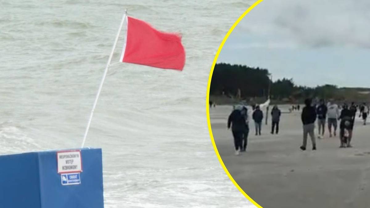 Czerwona flaga na plaży w Polsce, symbolizująca zakaz kąpieli, z widocznymi falami i kilkoma osobami w oddali.